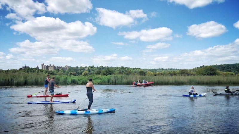 paddleboarders kayakers and motorboat on river arun