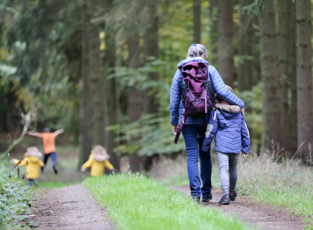 women and child walking in woods with other child playing